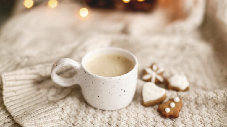 Tasse de café de noël avec des biscuits en forme de coeur et de sapin. Le tout est disposé sur un plaid et dans une ambiance confortable.